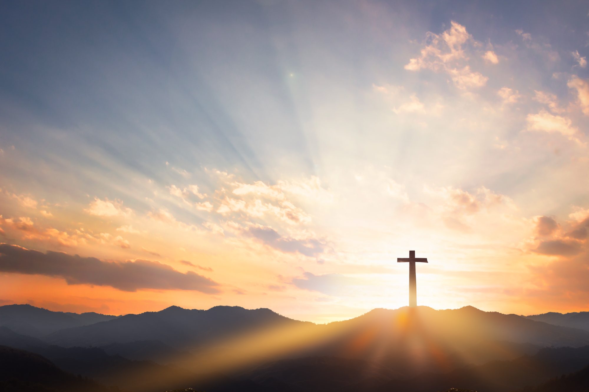 Cross silhouetted against a golden sunrise over misty mountains