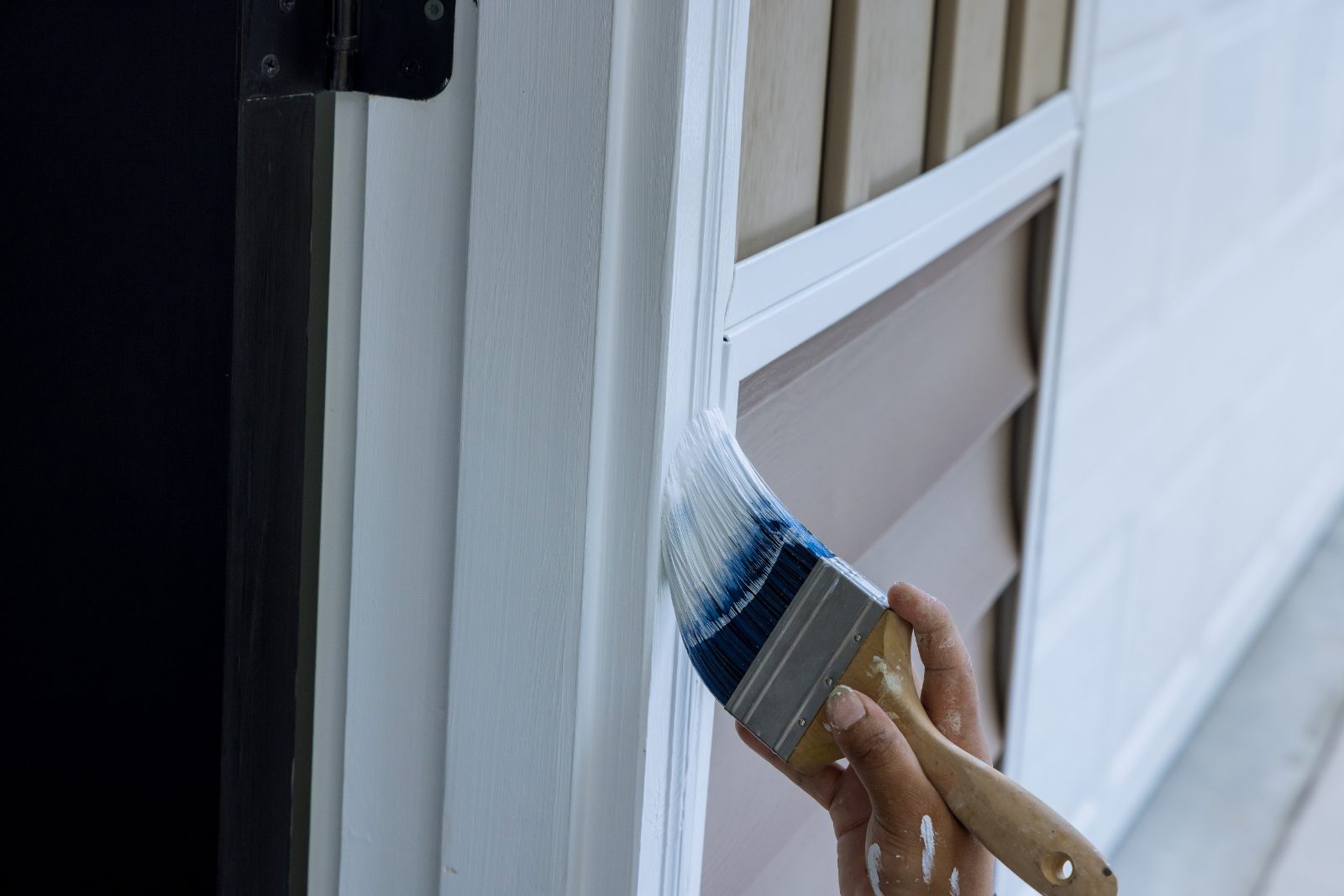 Worker painting white window trim with blue-bristled brush