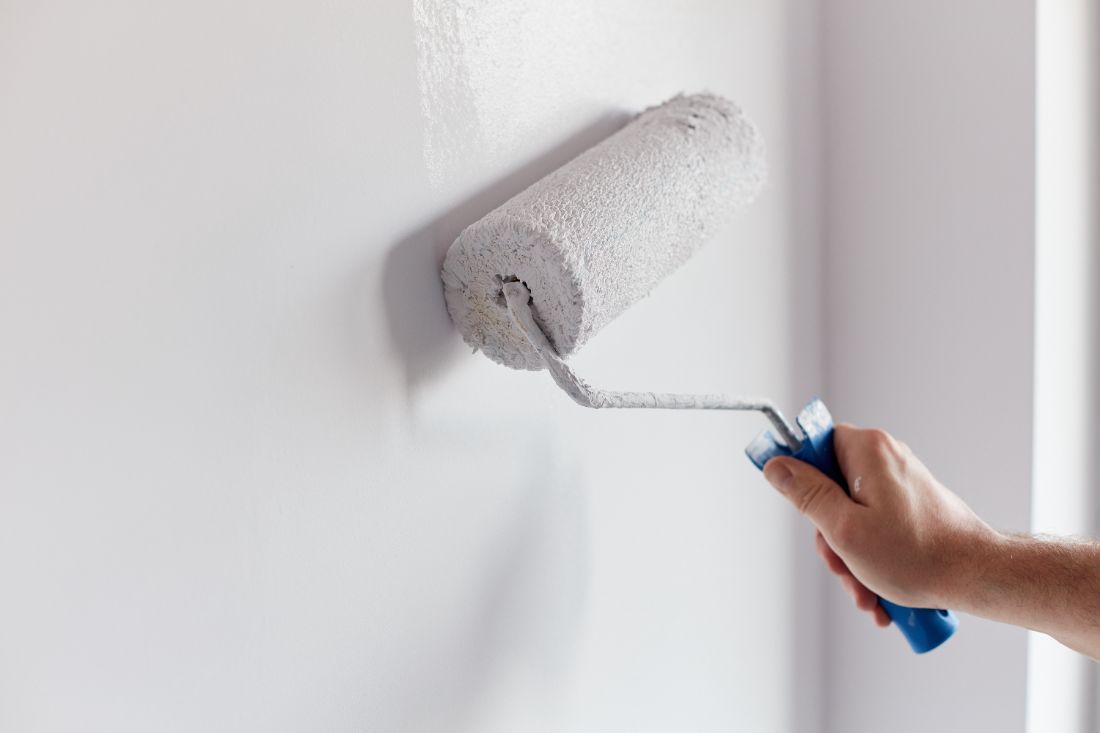 Person holding paint roller with blue handle against white wall